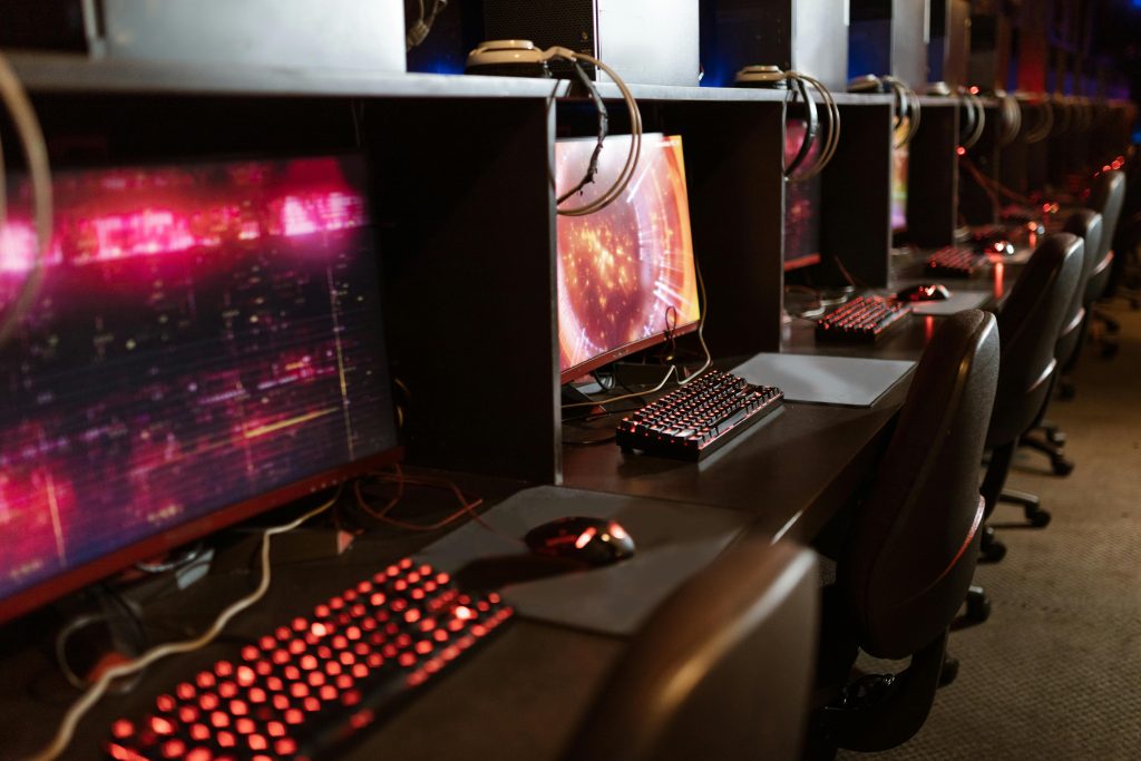 Row of gaming stations with illuminated keyboards and monitors in an esports arena.